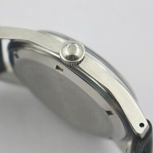 May include: Close-up of a silver wristwatch with a black leather band. The watch has a round face and a textured crown. The watch case is silver and the band is black.