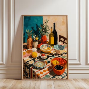 May include: A framed art print showing a still life composition. The image displays a table set with food items like fruit, olives, and cheese, plus bottles and vases. The tablecloth has a vibrant pattern. The color scheme includes blues, oranges, and yellows.