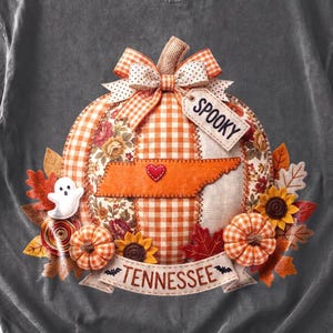 May include: A charcoal gray t-shirt featuring a large graphic of a patchwork pumpkin with orange gingham and floral patterns. The pumpkin has a bow, a tag reading SPOOKY, a Tennessee state outline with a red heart, and a banner reading TENNESSEE.