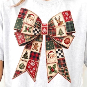 Puede incluir: Una camiseta blanca de manga corta con un gran gráfico central de un lazo decorativo hecho de varios cuadrados de patchwork. Los cuadrados muestran patrones con temática navideña que incluyen a Santa Claus, renos, hombres de jengibre, árboles y adornos.