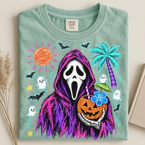 May include: A sage green t-shirt featuring a graphic of a hooded figure in a white mask holding a jack-o'-lantern drink with a straw and umbrella. The design includes a scribbled orange sun, blue palm tree, bats, stars, and small white ghosts.