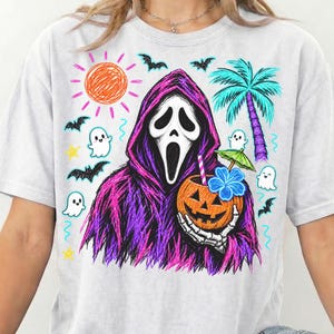May include: A light gray t-shirt featuring a graphic of a hooded figure with a white mask holding a carved pumpkin drink with a straw and umbrella. The design includes a bright orange sun, a blue palm tree, small white ghosts, and black bats.