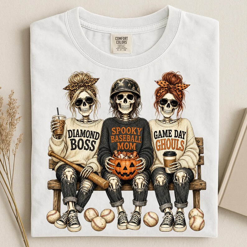 May include: A white t-shirt featuring a graphic of three skeletons sitting on a bench. The left skeleton wears a leopard print headband and holds a drink. The center skeleton wears a baseball helmet and holds a pumpkin. The right skeleton wears an orange headband and holds a coffee cup. Text reads DIAMOND BOSS, SPOOKY BASEBALL MOM, and GAME DAY GHOULS.