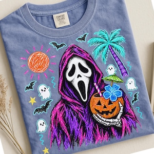 May include: A blue t-shirt featuring a graphic of a ghost-faced figure in a purple hooded robe holding a jack-o'-lantern with a tropical drink. The design includes a sun, palm tree, bats, stars, and small ghosts in a colorful, sketch-like style.