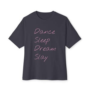 May include: A dark gray t-shirt with the words "Dance, Sleep, Dream, Slay" in pink script. The shirt has short sleeves and a crew neck.
