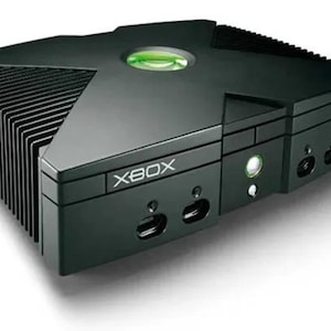 May include: Black Xbox games console with the word "XBOX" printed on the front. The console features a green power button and a green circular logo on top. The console has a distinctive rectangular shape with a ribbed side.
