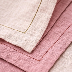 Peut inclure: Gros plan sur trois serviettes en lin dans les tons de rose et beige. La serviette supérieure est beige clair avec des coutures vert olive, tandis que les serviettes du milieu et du bas sont roses avec des coutures brun rougeâtre. Les serviettes sont pliées.