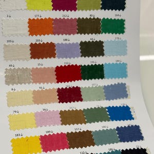 May include: A fabric color swatch card featuring a variety of fabric samples in various colors. The samples are arranged in rows and columns, showcasing shades of white, yellow, orange, pink, red, green, blue, and brown.