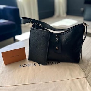 May include: Black leather shoulder bag with a matching wallet, both featuring embossed floral patterns. The bag has a long strap and a small tag with a gold logo. A beige dust bag and a small orange card with the words "LOUIS VUITTON" are also present.