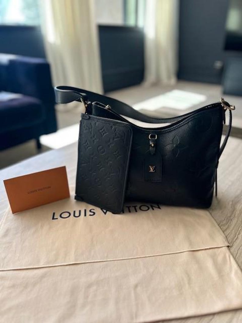 May include: Black leather shoulder bag with a matching wallet, both featuring embossed floral patterns. The bag has a long strap and a small tag with a gold logo. A beige dust bag and a small orange card with the words "LOUIS VUITTON" are also present.