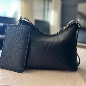 May include: Black leather shoulder bag and matching wallet. Both items feature a debossed monogram pattern. The bag has a curved shape with a shoulder strap. The wallet is rectangular and has a flap closure.
