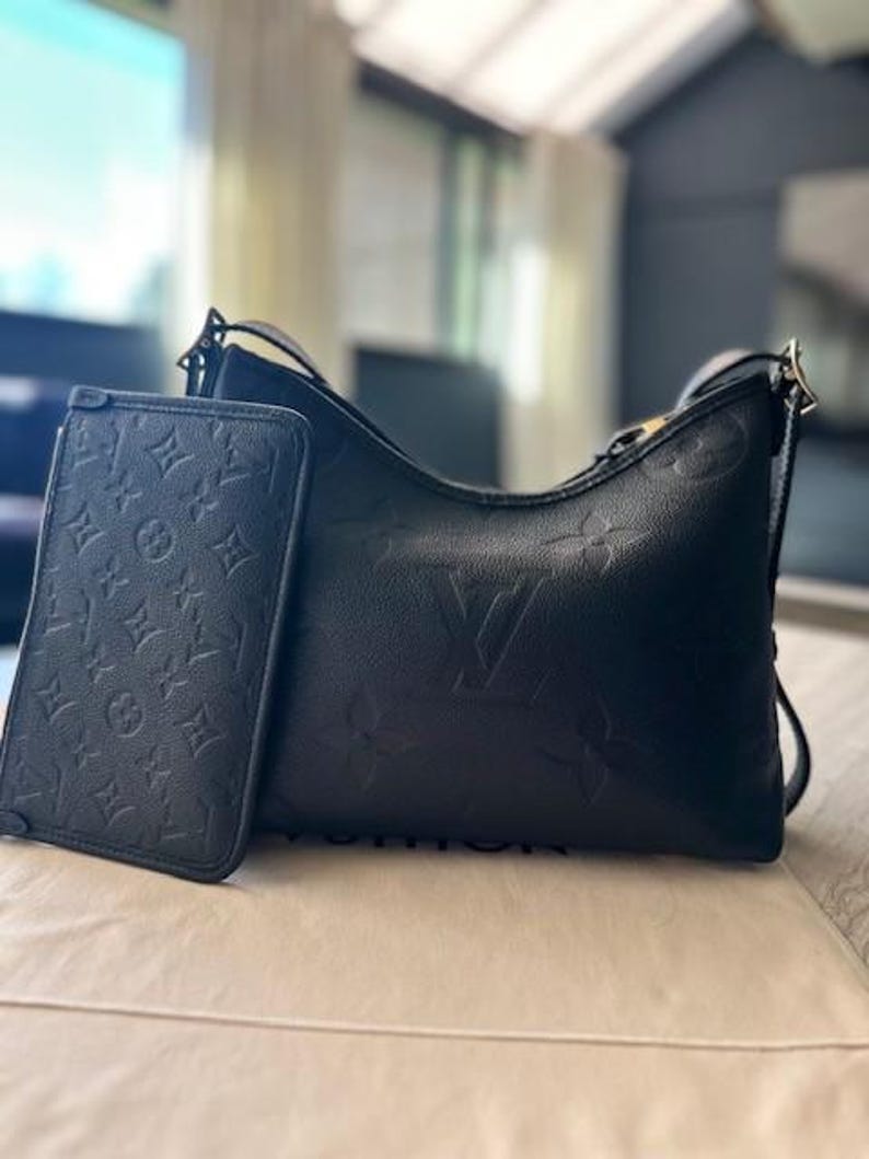 May include: Black leather shoulder bag and matching wallet. Both items feature a debossed monogram pattern. The bag has a curved shape with a shoulder strap. The wallet is rectangular and has a flap closure.