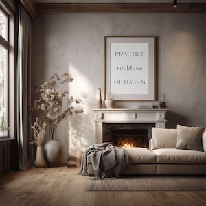 May include: A living room scene featuring a framed print with the words "PRACTICE reckless OPTIMISM." The room includes a fireplace, a beige sofa, and decorative vases with dried plants. The room has hardwood floors and a large window.