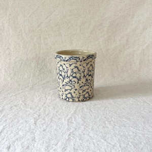 Puede incluir: Un tarro cilíndrico de gres con base color crema y un patrón moteado azul. El borde también es azul. Este clásico utensilio de cocina es adecuado para guardar utensilios o como elemento decorativo. Mide aproximadamente 10 cm de alto.