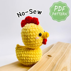 Puede incluir: Un pollo de ganchillo amarillo hecho a mano con cresta y barbilla rojas. El pollo tiene ojos negros y un pequeño rubor rosado. Las palabras "No-Sew" y "PDF PATTERN" son visibles en la imagen.