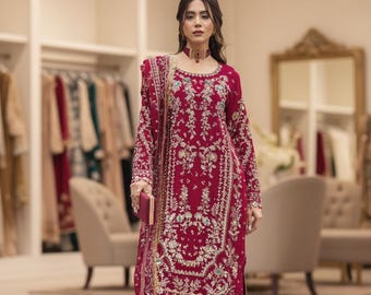 May include: A deep magenta long-sleeved tunic featuring intricate gold embroidery and beadwork, paired with matching wide-leg pleated trousers and a coordinating embroidered dupatta. A matching choker necklace and a small magenta clutch are included.