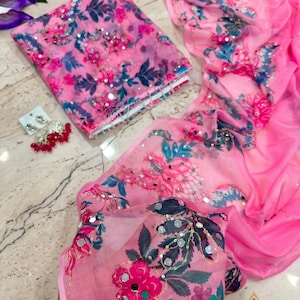 May include: A bright pink sheer fabric garment featuring a floral print in shades of dark blue, magenta, and light pink, accented with small reflective mirror embellishments and sequins. A pair of matching dangling earrings with red beads is included.