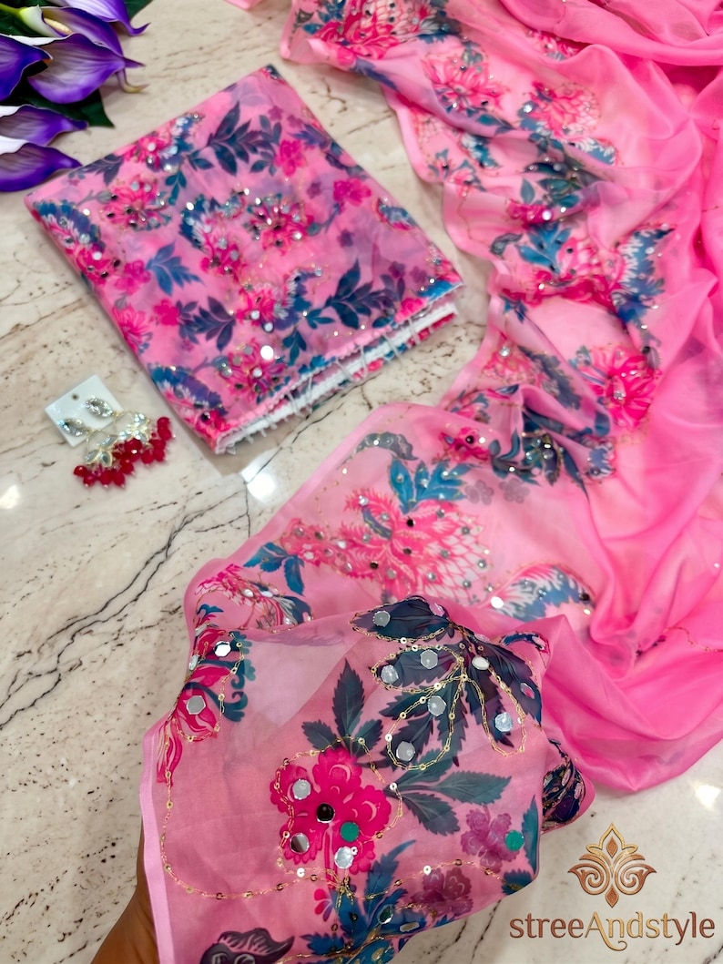 May include: A bright pink sheer fabric garment featuring a floral print in shades of dark blue, magenta, and light pink, accented with small reflective mirror embellishments and sequins. A pair of matching dangling earrings with red beads is included.