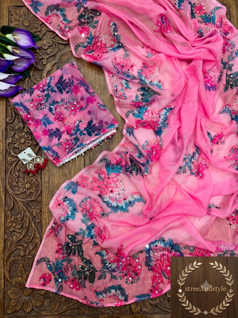 May include: A bright pink sheer fabric garment featuring a floral pattern in shades of dark blue, magenta, and white, accented with small reflective sequins. A pair of matching earrings with red beads and gold-tone metal accents is included.