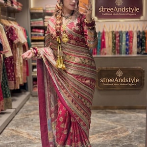 May include: A deep magenta saree featuring intricate gold embroidery, horizontal striped patterns, and floral motifs. The garment includes a long-sleeved blouse with matching embellishments, a draped pallu, and a border with detailed gold thread work.