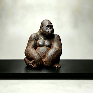 Puede incluir: Una detallada escultura de gorila marrón en posición sentada, con una expresión pensativa. El gorila está colocado sobre una estantería rectangular negra sobre un fondo neutro. La escultura muestra pelaje texturizado y definición muscular.
