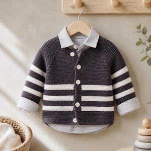 May include: A dark gray knit cardigan with white horizontal stripes and a collared shirt underneath. The cardigan has long sleeves and is buttoned up. The shirt collar and cuffs are striped. The cardigan is hanging on a wooden hanger.