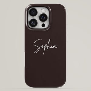 Puede incluir: Una funda de smartphone de color marrón oscuro con el nombre Sophia escrito en una fuente cursiva blanca. La funda tiene un recorte rectangular en la esquina superior izquierda para un sistema de triple cámara y flash, mostrando la parte trasera.