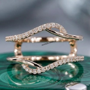 Op de afbeelding: Een roségouden ring met een gebogen ontwerp, bezet met kleine, sprankelende diamanten. De ring heeft de tekst "AVENZA JEWELS". De ring staat tegen een groene en grijze achtergrond.