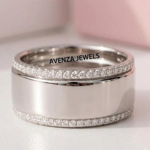 May include: A wide, silver-colored ring with a polished center band and two rows of small, sparkling stones. The text "AVENZA JEWELS" is printed on the ring.