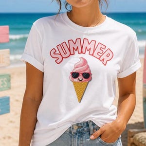 Op de afbeelding: Wit T-shirt met het woord "SUMMER" in rode bubbelletters boven een cartoon ijsje met zonnebril. Het ijsje is roze met een wafel. Het shirt wordt gedragen met een spijkerbroek short.