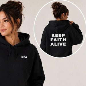 Op de afbeelding: Een zwarte hoodie met de witte tekst KFA op de borst. De achterkant van de hoodie toont de witte tekst KEEP FAITH ALIVE in een vetgedrukt schreefloos lettertype. Het kledingstuk is voorzien van een capuchon met bijpassende zwarte trekkoorden.