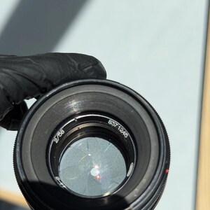 May include: A black camera lens with the numbers "2/58" and "837 1245" visible. The lens has a series of concentric rings and a red dot. The aperture blades are partially closed, creating a star-like pattern.