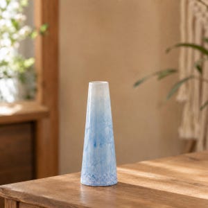 Peut inclure: Un vase conique élancé présentant une silhouette lisse et effilée. La surface affiche un motif de couleur dégradé, passant d'un blanc éclatant au sommet étroit à un bleu ciel vibrant et tacheté à la base large, avec des textures cristallines.
