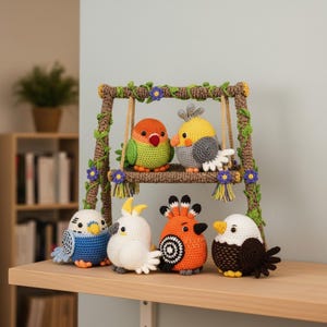 May include: A collection of six colorful, crocheted bird figurines. Two birds sit on a brown swing decorated with green vines and purple flowers. The other four birds are displayed below. Each bird has unique colors and patterns, including blue, white, orange, and brown.