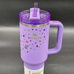 Peut inclure: Un gobelet Stanley Quencher H2.0 Flowstate violet avec une poign&eacute;e et une paille. Le gobelet pr&eacute;sente un motif d'&eacute;toiles et le logo Stanley. Le gobelet est de 1,18 L.