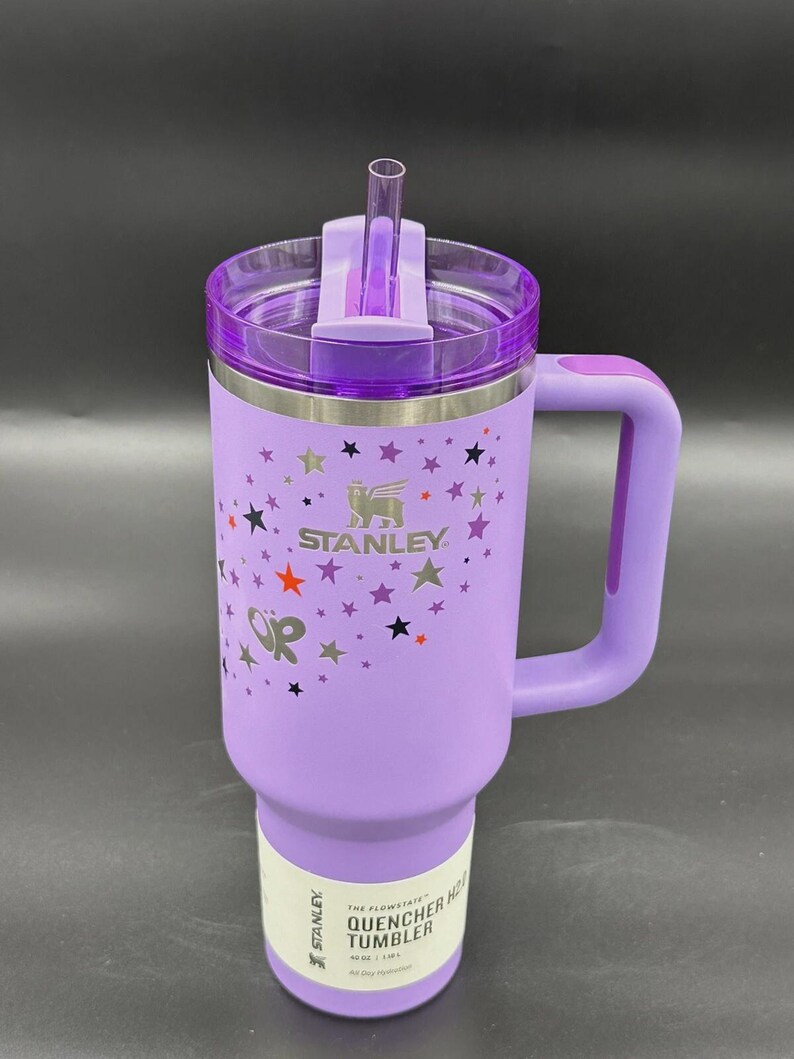 Peut inclure: Un gobelet Stanley Quencher H2.0 Flowstate violet avec une poign&eacute;e et une paille. Le gobelet pr&eacute;sente un motif d'&eacute;toiles et le logo Stanley. Le gobelet est de 1,18 L.