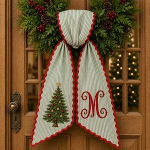 May include: A light green and white striped fabric door hanger with a scalloped red edge. The left side features a decorated Christmas tree with red and gold ornaments, while the right side displays a large, embroidered red letter M monogram.