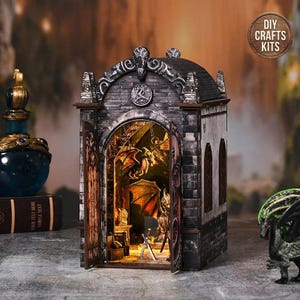 May include: A miniature, illuminated fantasy diorama featuring a stone building with open doors. Inside, a detailed scene with dragons, swords, and a warm glow. The diorama is a DIY craft kit, as indicated by the text on the circular label.