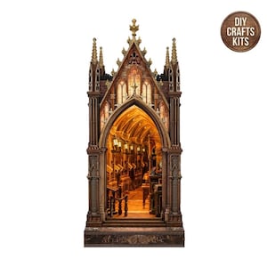 May include: A brown, gothic-style miniature library book nook kit featuring pointed arches, tall spires, and an illuminated interior with detailed shelves and furniture. The base includes the text "THE LIBRARY" and a circular badge reads "DIY CRAFTS KITS".