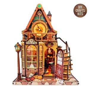 May include: A wooden model kit of a building titled The Pavilion of Time, featuring a large clock face on the upper level, a street lamp, a spiral staircase, and an open door. The structure includes interior lighting, miniature pumpkins, and decor.