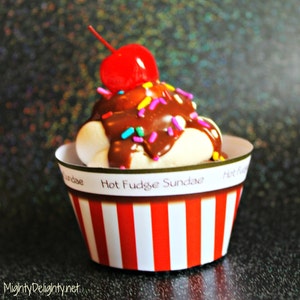 May include: A cupcake decorated to look like a hot fudge sundae. The cupcake is topped with white frosting, chocolate sauce, sprinkles, and a red cherry.