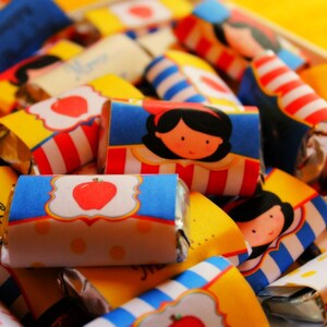 Könnte beinhalten: Nahaufnahme von mehreren kleinen verpackten Süßigkeiten mit bunten Designs, die ein Cartoon-Bild von Schneewittchen, Äpfeln und den Worten "Happy Birthday" zeigen.