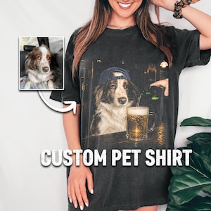 May include: A charcoal gray t-shirt featuring a graphic print of a dog wearing a blue baseball cap sitting at a bar next to a glass of beer. A small inset image shows the original dog photo. The text CUSTOM PET SHIRT is printed below.