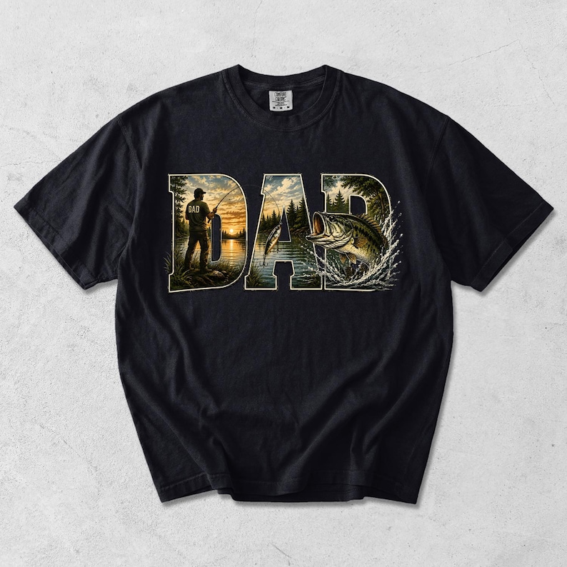 May include: Black t-shirt with a graphic design featuring the word "DAD" in a stylized font. The letters are filled with a fishing scene, including a person fishing at sunset and a leaping fish. The shirt is made of a soft material.