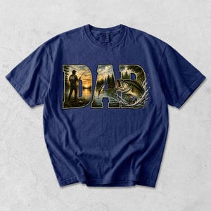 May include: Navy blue t-shirt with the word "DAD" in a nature-themed design. The letters feature a fisherman, a lake, and a leaping bass. The shirt is a comfortable, casual wear item.
