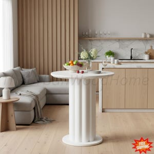 May include: A white circular dining table featuring a fluted pedestal base. The table surface is smooth and round, supported by a thick, vertically ribbed column that rests on a circular base plate, creating a clean and structural appearance.