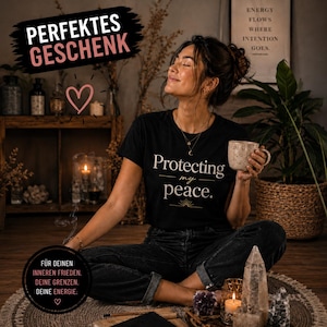 Könnte beinhalten: Schwarzes T-Shirt mit dem weißen Schriftzug „Protecting my peace“. Das Bild enthält Text auf Deutsch, ein Herzsymbol und eine Frau, die eine gesprenkelte Tasse hält. Der Hintergrund zeigt Pflanzen, Kerzen und Kristalle.