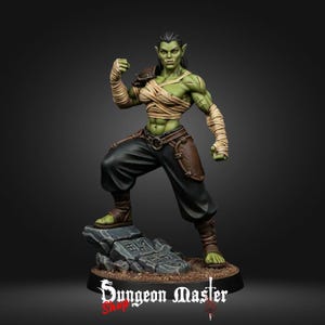May include: A detailed figurine of a female orc warrior, posed in a fighting stance. The orc has green skin, black hair, and is wearing black pants, brown leather armor, and bandages. The base of the figurine has the text "Dungeon Master Shop".