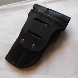 May include: Black leather holster with a flap and three cutouts. The holster has two silver rivets.