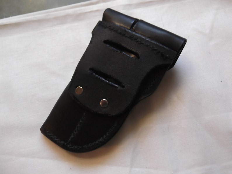 May include: Black leather holster with a flap and three cutouts. The holster has two silver rivets.